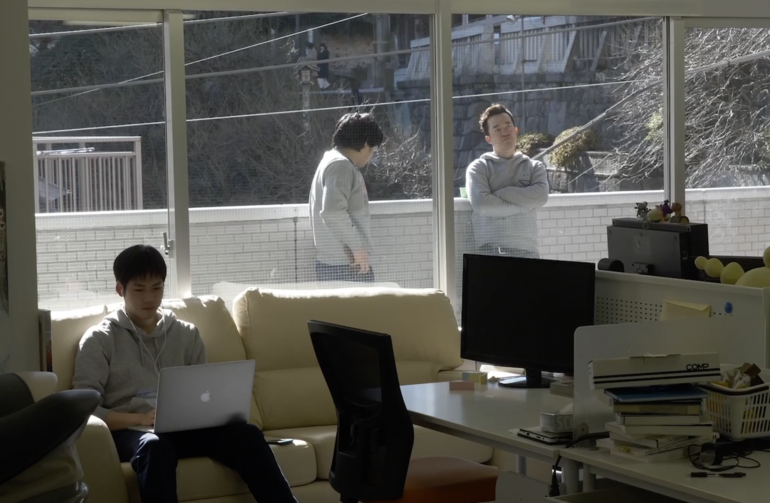 ベランダで社員の言葉に耳を傾け、腕組みする田中社長（右）